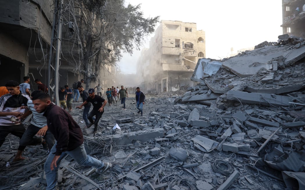 People run for cover following an Israeli strike that targeted a building in the Bureij camp for Palestinian refugees in the central Gaza Strip on October 19, 2025. Gaza's civil defence agency said a series of Israeli air strikes on October 19 killed at least 11 people across the territory, as Israel and Hamas traded blame for violating a ceasefire. (Photo by Eyad BABA / AFP)