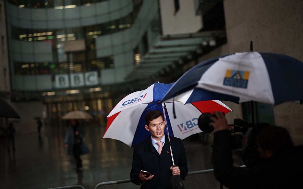 Members of the media work in the rain outside the entrance to the BBC in London on November 10, 2025. The outgoing CEO of BBC News said on November 10, 2025 that the broadcaster was "not institutionally biased", after she resigned over accusations that it had misleadingly edited a speech by Donald Trump. (Photo by HENRY NICHOLLS / AFP)