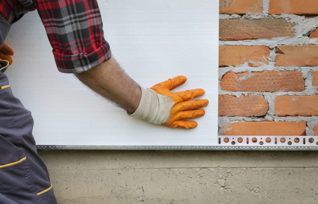 Worker placing styrofoam, polystyrene thermal insulation to brick wall, house renovation
