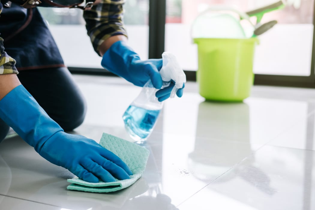 Husband housekeeping and cleaning concept, Happy young man in blue rubber gloves wiping dust using a spray and a duster while cleaning on floor at home.