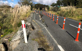 A slump on the side of a two lane road. It has been closed off with orange marker poles.