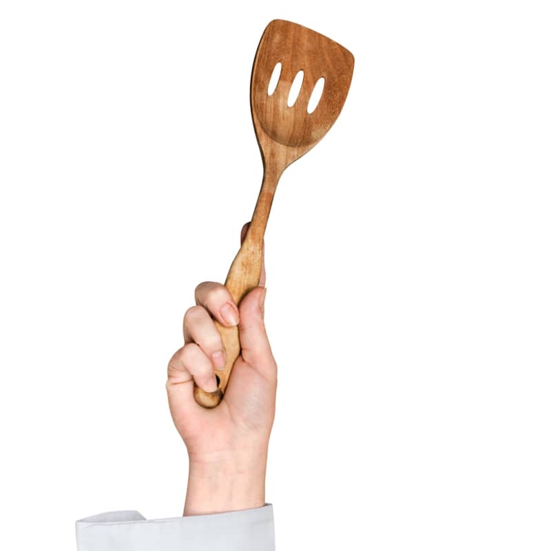 A hand holds a wooden spatula high in the air.