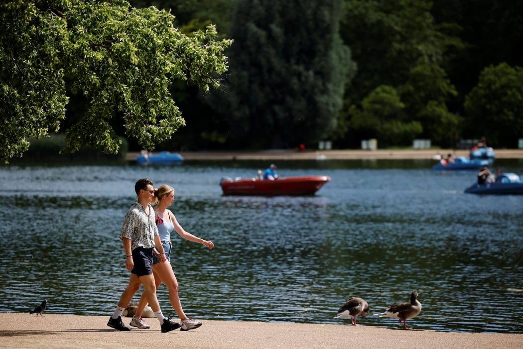 People walk in the sunshine in past the boating lake in Hyde Park in London on 14 June 2021.