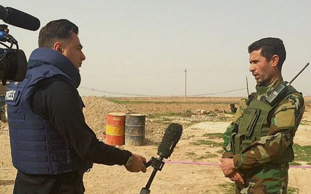 Imran Khan wearing flak jacket holds mic out as he interview Iraqi officer