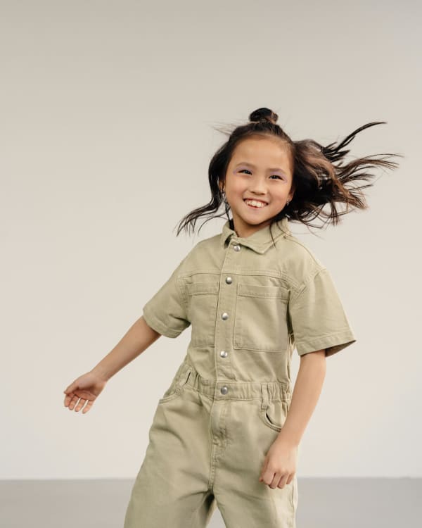 A happy Asian girl in a jumpsuit smiles as her hair flies around her head.