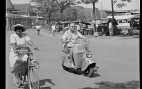 Street scene, Woman riding her bicycle and man riding his motor scooter, Papeete, Tahiti 1952.