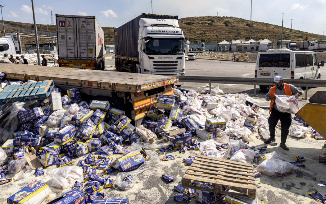 A worker clears spilled goods away from damaged trailer trucks that were carrying humanitarian aid supplies on the Israeli side of the Tarqumiyah crossing with the occupied West Bank on May 13, 2024, after they were vandalised by other activists to protest against aid being sent to the Gaza Strip.