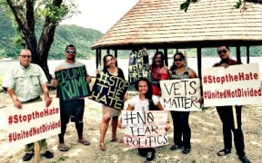 Protesters at Utulei Beach hold signs accusing Donald Trump of divisive politics and disparaging remarks.