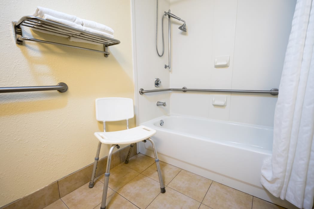 Handicap Hotel Bathroom with Shower Bathtub Hand Rails and a Chair