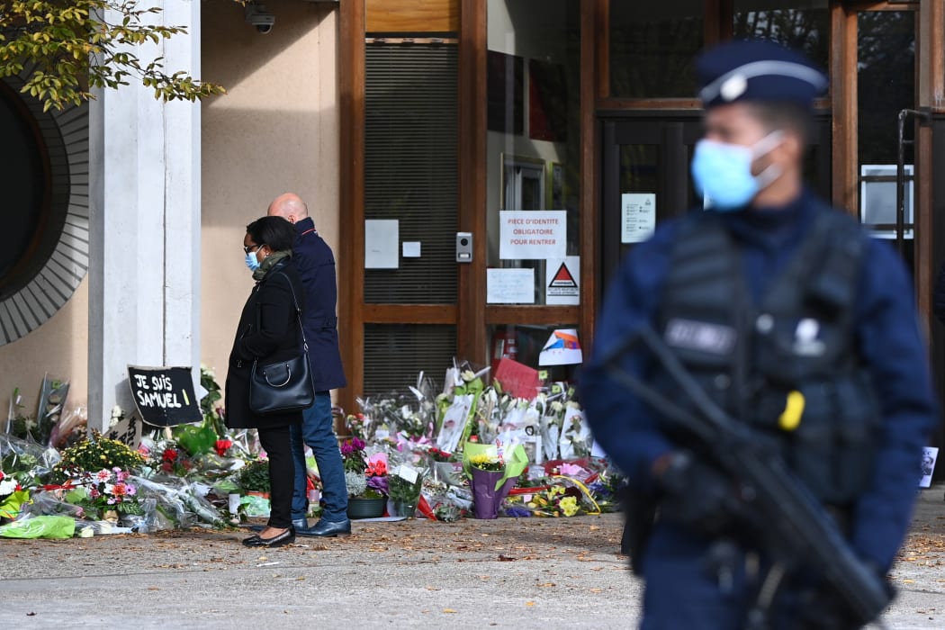 People look at flowers layed outside the Bois d'Aulne secondary school in homage to slain history teacher Samuel Paty.