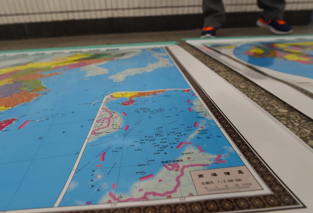 In this photo taken on June 15, 2016 a vendor stands behind a map of China including an insert with red dotted lines showing China's claimed territory in the South China Sea, in Beijing.