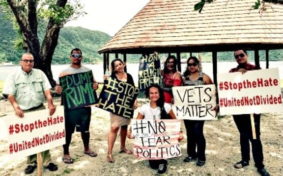 Protesters at Utulei Beach hold signs accusing Donald Trump of divisive politics and disparaging remarks.