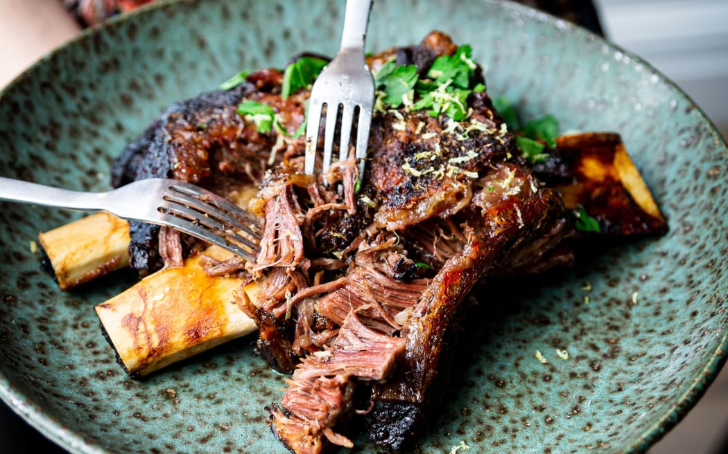 A plate of slow cooked short ribs, being pulled apart by two forks.