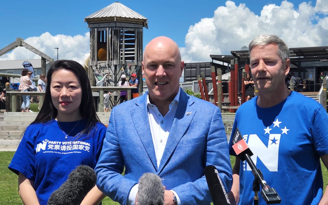 Incoming Prime Minister Christopher Luxon (C), with Nancy Lu (L) and MP Andrew Bayly (R) at a media standup in Port Waikato.