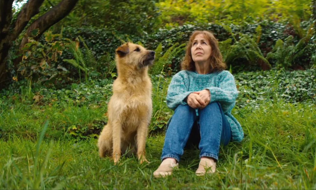 Film still from the Irish movie Róise and Frank showing Frank the dog and Róise sitting together on the grass