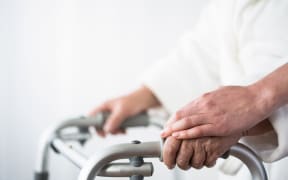 Elderly person using walking aid with help of person.