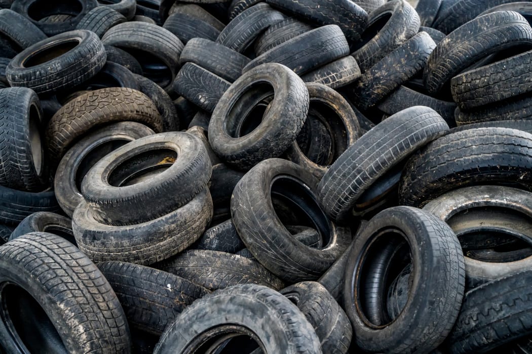 Big pile of automobile tires on the broken-down plant. Many black rubber tyres on the ground inside the old huge empty building.