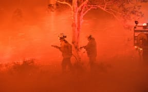 Firefighters struggling against strong winds and flying embers in an effort to secure nearby houses from bushfires near the town of Nowra in the Australian state of New South Wales on 31 December.