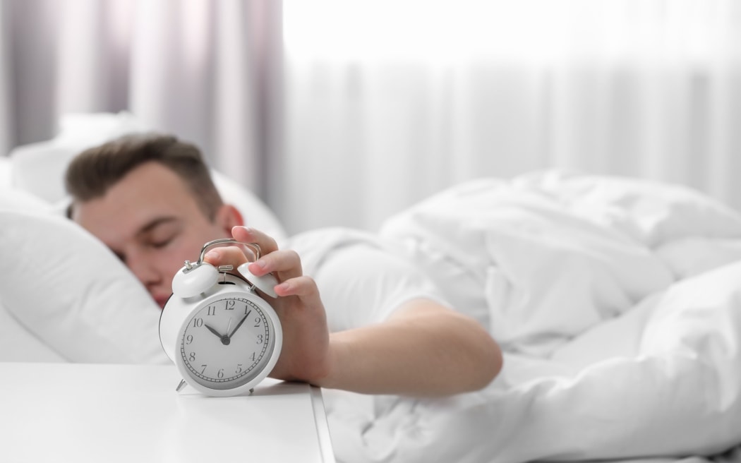 Man sleeping and turning off alarm clock