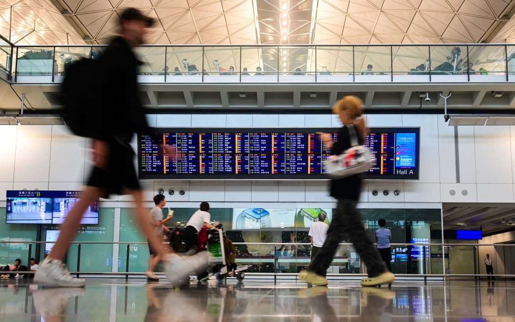 Passengers walk past a flight information board at the Hong Kong International Airport.