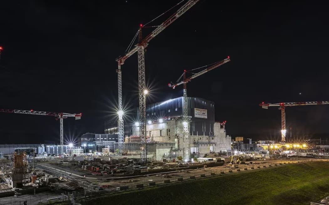 Cranes soar over ITER's main building, lit up at night.