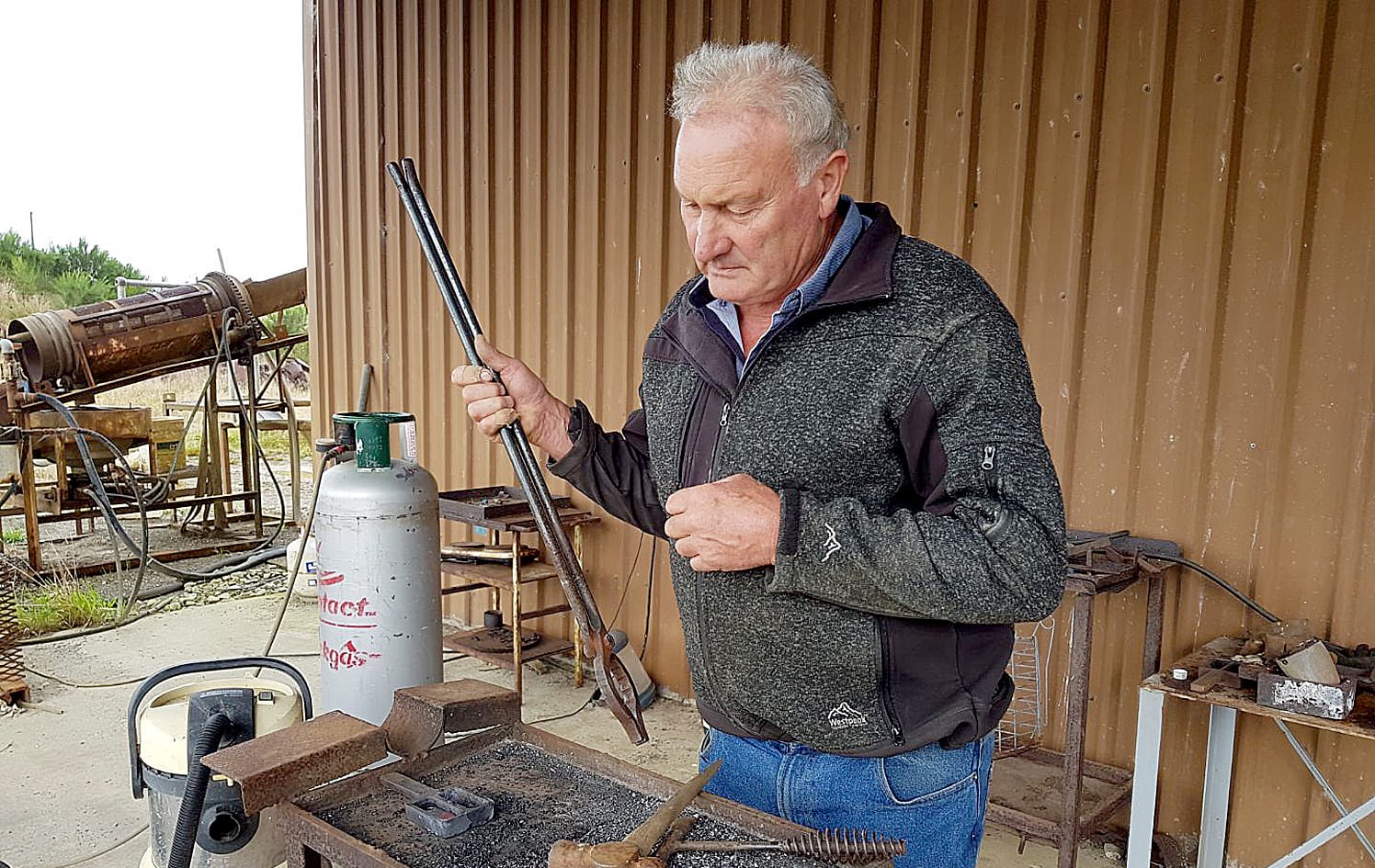 Allan Birchfield winnows the tiny gold flakes on a piece of paper to shake any dirt out; the flakes are smelted in a ceramic pot (crucible) in a small gas-fired furnace.