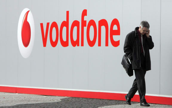 man with mobile phone walking past Vodafone sign