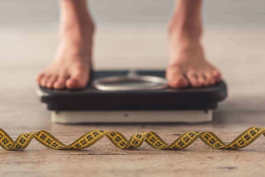 Person standing on weigh scales, tape measure in the foreground.