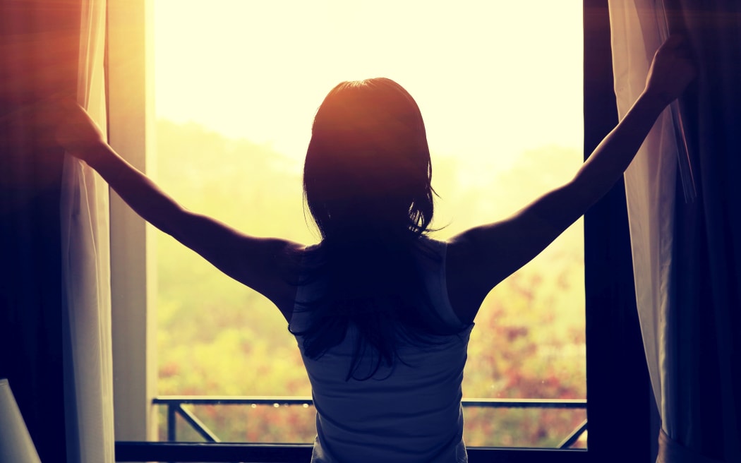 young woman opening curtains in a bedroom