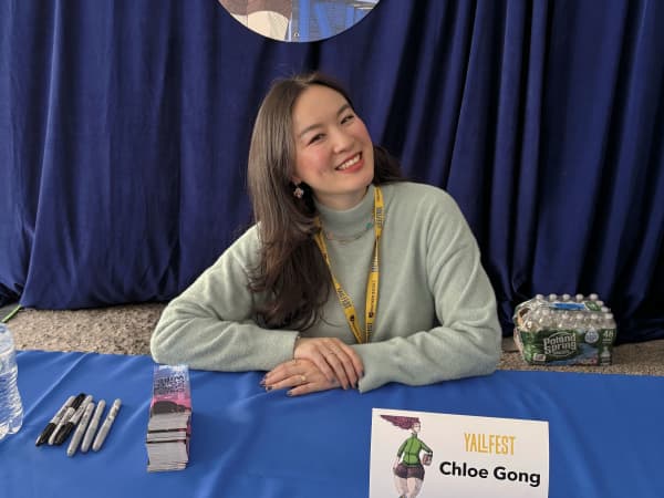 Chloe Gong sits on a table smiling as she gets ready to sign fans' books.
