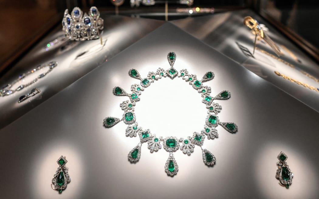 A lavish jewelled necklace lies with some matching earrings on an illuminated surface.