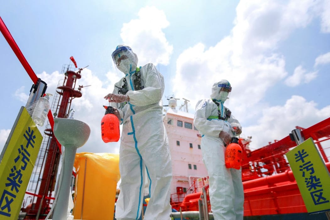 Police officers wearing protective gear spray disinfectant at Nanjing port.