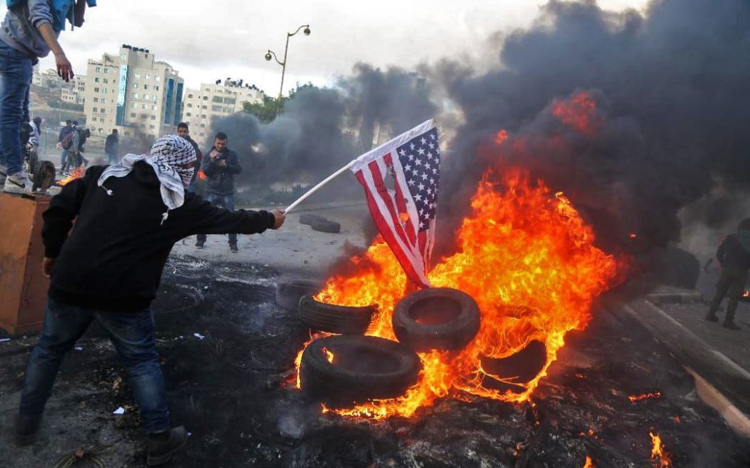 A Palestinian protester sets alight an America flag during clashes with Israeli troops at a protest against US President Donald Trump's decision to recognize Jerusalem as the capital of Israel.