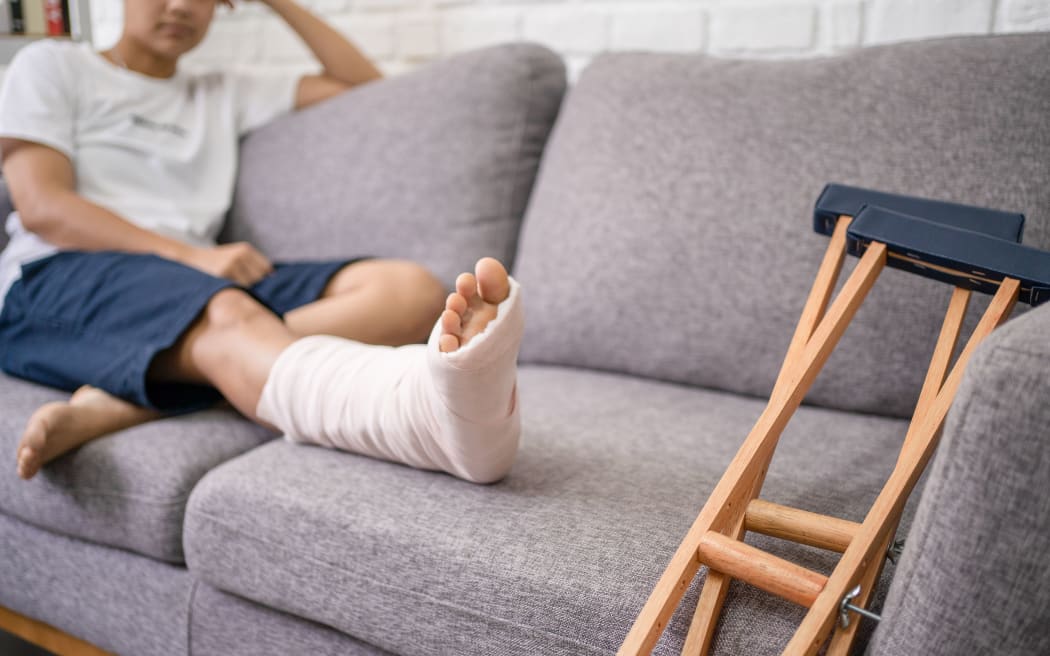 Young Asian man with a broken leg sitting on the sofa. Close up of the crutch.