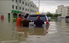 In this video grab from AFPTV, people push a stranded car along a flooded street in Dubai on 16 April, 2024.
