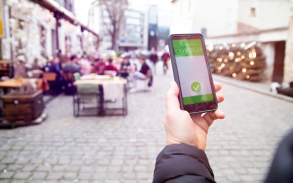 Vaccinated person using a digital vaccination or immunisation certificate on a smartphone at a restaurant terrace.