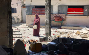 A woman carries a plastic container at Mustafa Hafez school, sheltering Palestinians displaced by the war, after the school was hit during an overnight Israeli strike in Gaza City, on July 3, 2025, amid the ongoing conflict between Israel and the Palestinian Hamas militant group. (Photo by Omar AL-QATTAA / AFP)