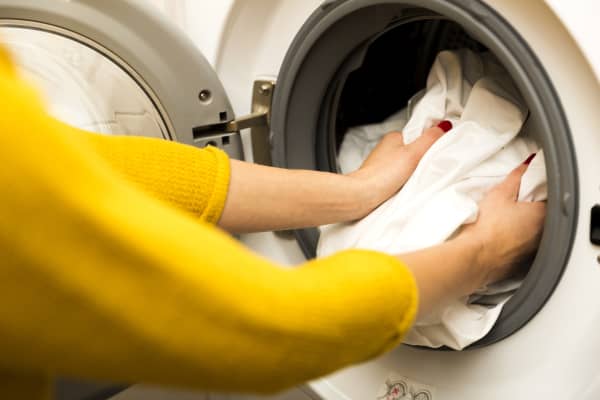 Woman hand loading dirty clothes in washing machine.