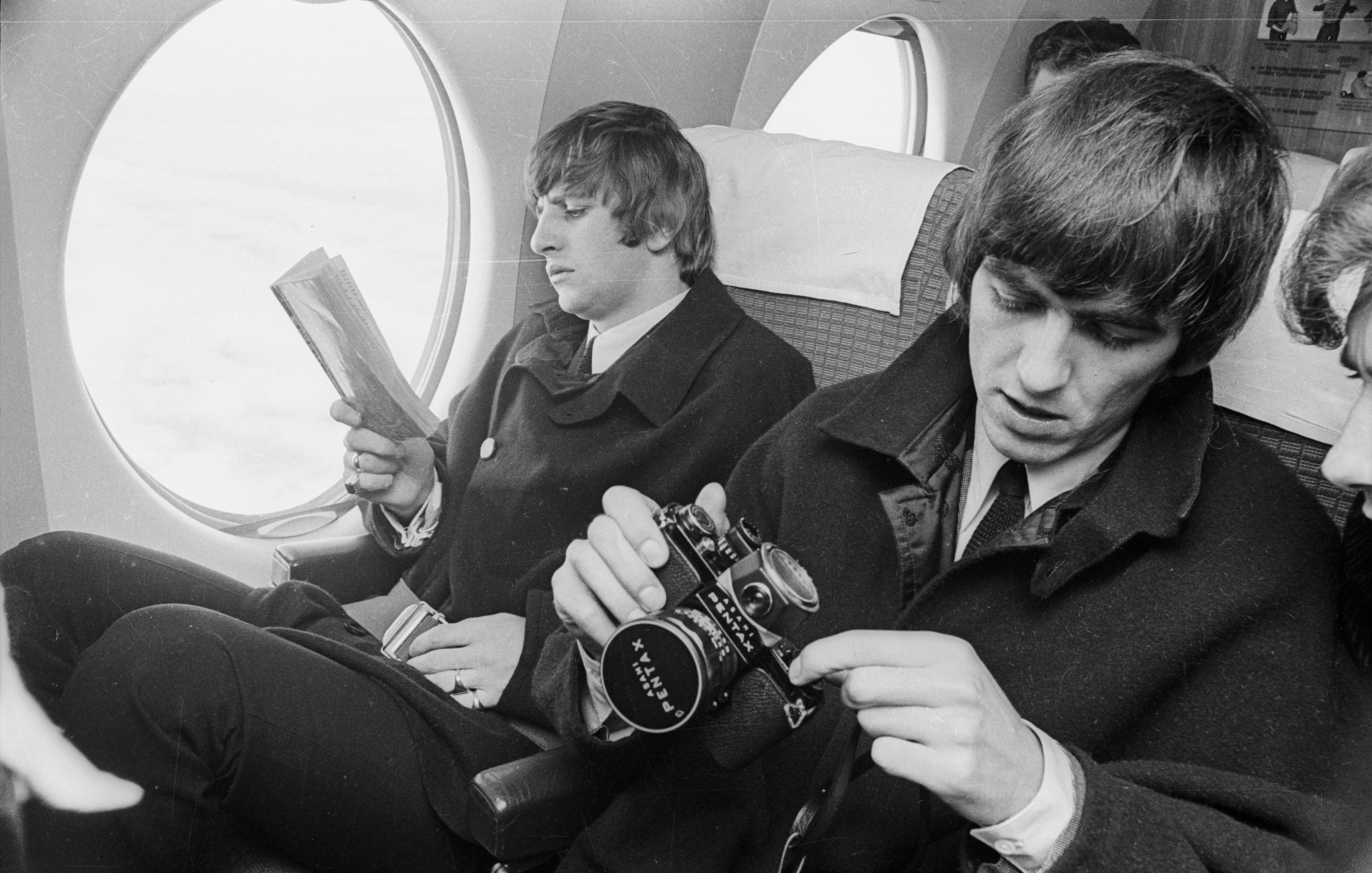 Beatles Ringo Starr and George Harrison on a plane with book and camera.