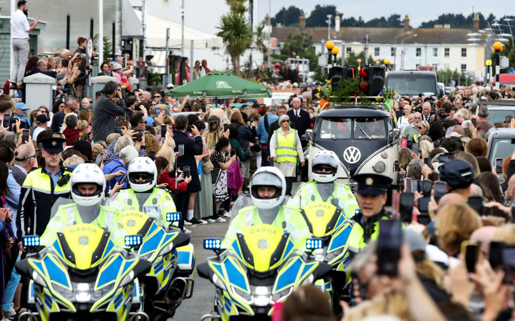 People gather to pay a tribute during the funeral procession of late Irish singer Sinead O'Connor, outside the former home in Bray, eastern Ireland, ahead of her funeral on August 8, 2023. A funeral service for Sinead O'Connor, the outspoken singer who rose to international fame in the 1990s, is to be held on Tuesday in the Irish seaside town of Bray. (Photo by PAUL FAITH / AFP)