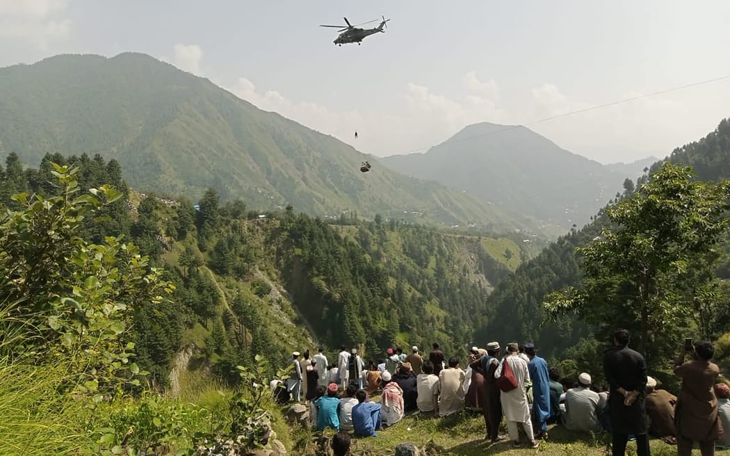 People watch a helicopter rescue mission to recover children and an adult stuck in a chairlift at Pashto village in the mountainous Khyber Pakhtunkhwa province, 22 August, 2023.