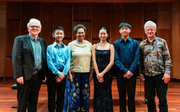 The finalists and adjudicators for the National Concerto Competition 2026 stand next to each other on a wooden stage, smiling. Their names are Mark Walton, Ryan Yeh, Wilma Smith, Lorna Zhang, Hayden Chiu, and Donald Maurice.