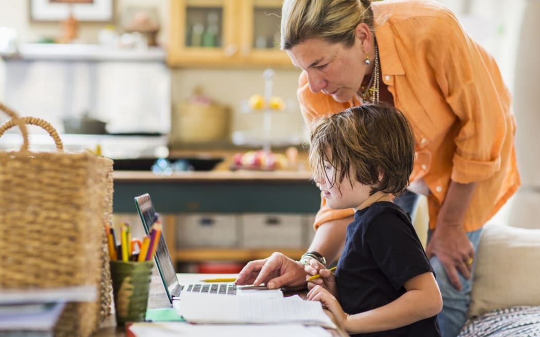 [New Mexico, United States] Adult woman helping her six year old son with a remote learning session on a laptop, using a touchpad.