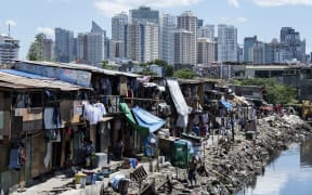 People living in a settlement walk about, as the skyline of Manila's financial district is seen in the background, on August 17, 2017.
