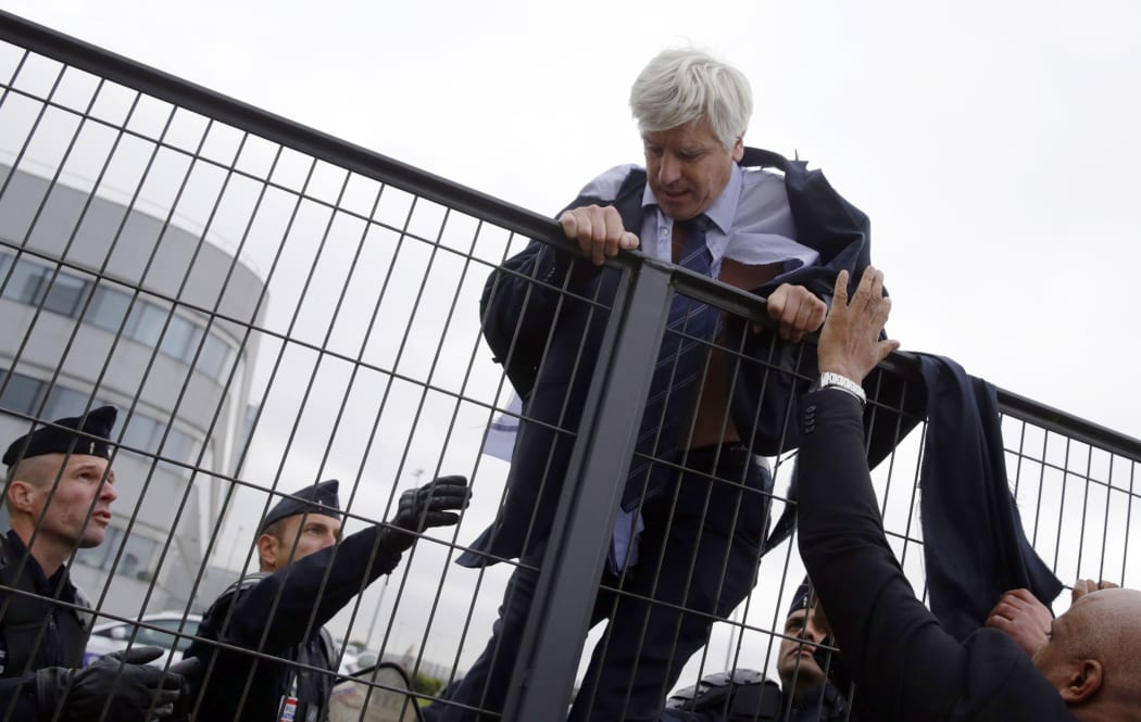 Air France's director of long-haul flights, Pierre Plissonnier is helped by security and police officers to climb over a fence.