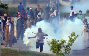 A Pakistani supporter of the Canadian cleric Tahir ul Qadri returns a tear gas shell towards police during clashes with security forces.