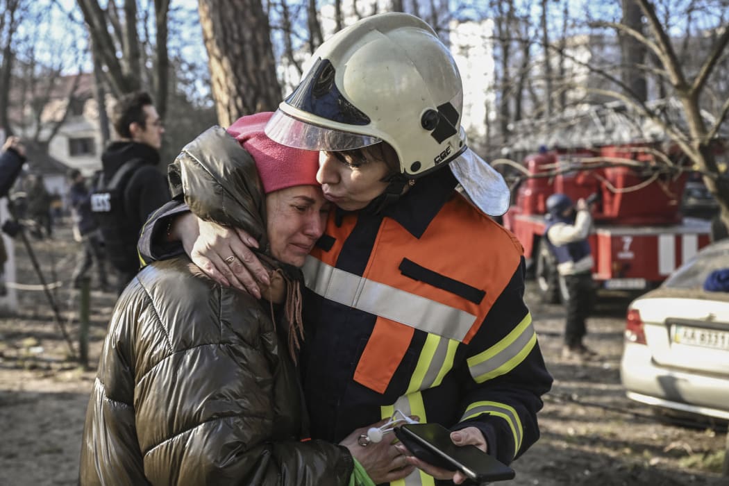 An evacuated resident is comforted by a rescue worker outside a burning apartment building in Kyiv on 15 March 2022, after strikes on residential areas.