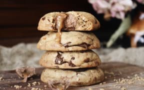 A stack of cookies studded with broken up caramel Easter eggs and tamari almonds on a board.