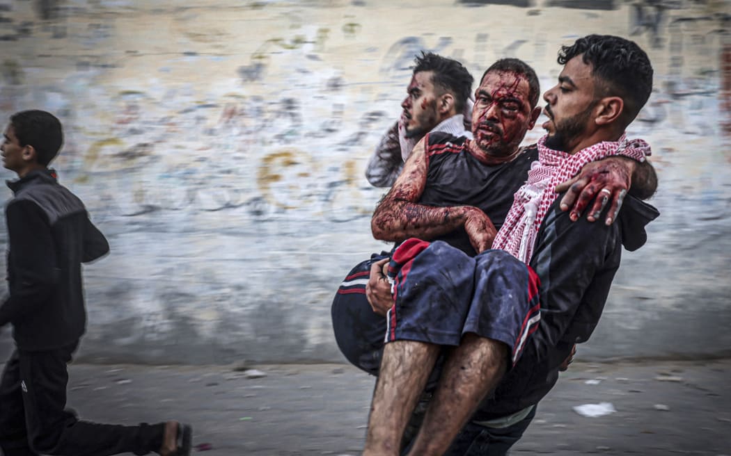 EDITORS NOTE: Graphic content / A Palestinian man carries an injured man as people flee following an Israeli strike in Rafah in the southern Gaza Strip on November 23, 2023, amid ongoing battles between Israel and the Palestinian militant group Hamas. (Photo by Mohammed ABED / AFP)