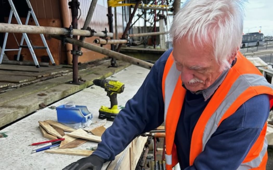 Peter McCurdy is working on the SS Toroa. He's wearing a high vis jacket and holding a plank in place.